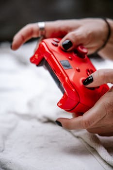 Close-up of a person holding a red gaming console controller with manicured nails.