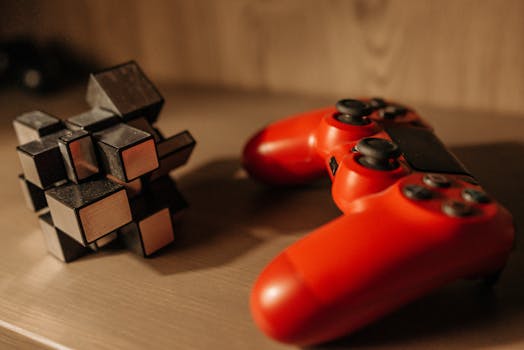 Close-up of a red game controller and 3D cube puzzle on a wooden surface.