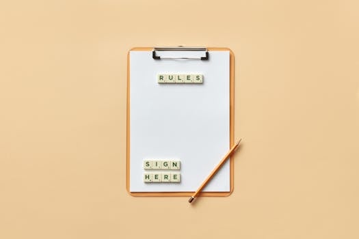 Flat lay of clipboard with letter tiles spelling 'rules' and 'sign here', accompanied by pencil on beige background.