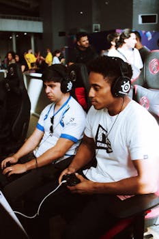 Two gamers intensely focused during a competitive esports event, wearing headsets and using controllers.