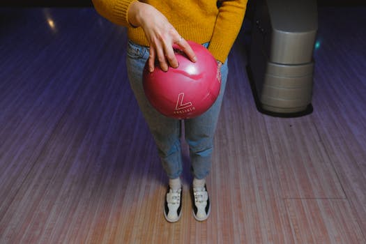 Woman in casual clothing holding a pink bowling ball at an indoor bowling alley.