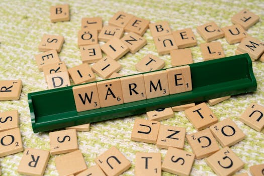 Wooden alphabet tiles spelling 'Wärme' on a green tray, scattered on fabric.